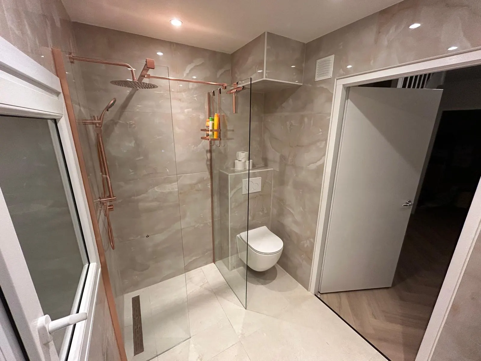 Gerenoveerde badkamer met marmerlook tegels en koperen regendouche in Delft